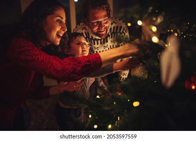 Family of three preparing fir tree for Christmas eve celebrations at home. Family decorating Christmas tree together at home. - Powered by Shutterstock