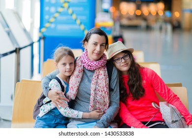 A Family Of Three Sitting In A Recreation Area At The Airport
 - Mother And Two Daughters In Airport Departure Lounge Waiting For A Flight