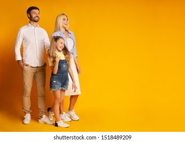 Family Of Three Smiling Looking At Copy Space Standing On Yellow Background. Studio Shot