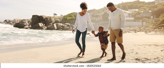Family of three taking a walk along the sea shore. Man and woman holding hands with their son and walking on beach.
