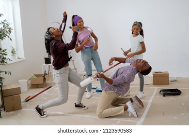 Family throws a party during apartment renovation, taking a break from painting walls, parents with children sing to rollers, dance, man falls on his knees and pretends to play guitar