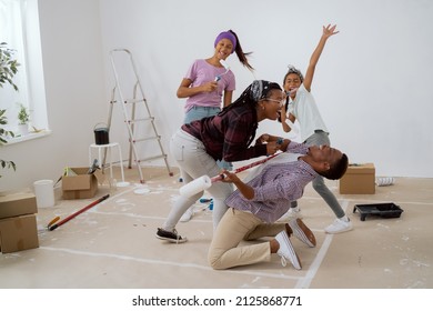 Family throws a party during apartment renovation, taking a break from painting walls, parents with children sing to rollers, dance, man falls on his knees and pretends to play guitar