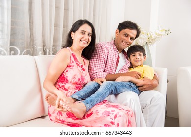 Family Time - Candid Portrait Of Smart Indian Family Of Three While Sitting On Sofa. Indian Or Asian Family Group Photo. Selective Focus