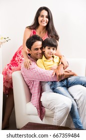 Family Time - Candid Portrait Of Smart Indian Family Of Three While Sitting On Sofa. Indian Or Asian Family Group Photo. Selective Focus