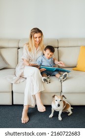 Family time at home.  Beautiful smiling blond woman, 2 yers old boy and dog together in living room reading books. Happy relaxed moment. upbringing and education of the child. Vertical composition