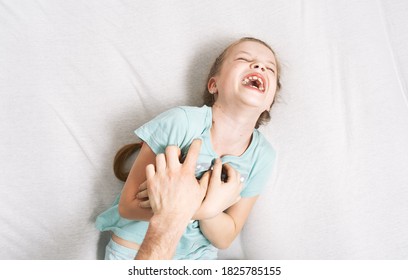 Family time: a little girl lies on the bed and laughs cheerfully because of the tickling of her father.
