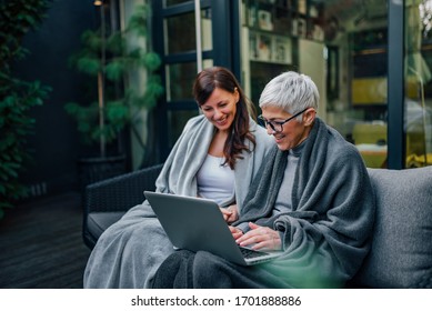 Family Time. Mother And Daughter Looking At Laptop At Modern Home Garden, While Sitting Covered In Blankets.