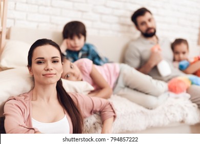 Family Tired Of Cleaning Is Sitting On The Couch In The Apartment. They Are Looking Into The Camera. The Family Has Five People, Two Adults And Three Children.