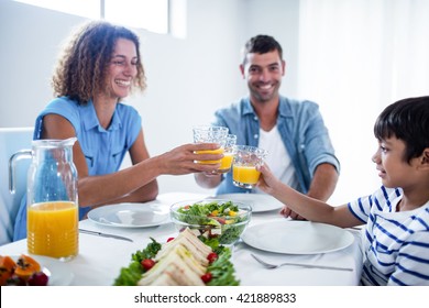 Family Toasting Glasses Of Orange Juice While Having Breakfast At Home