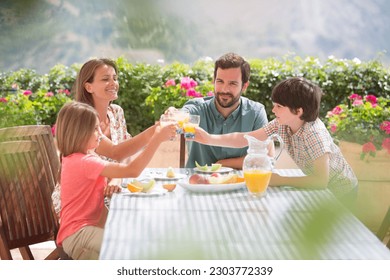 Family toasting orange juice glasses at table in garden - Powered by Shutterstock