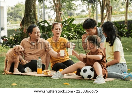 Family toasting with paper cups of juice when having picnic in park