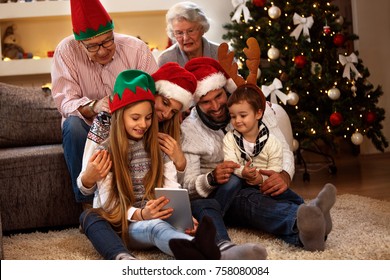 Family Together In Christmas Eve Looking Photos On Tablet At Home