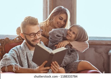 Family Togetherness. Mom, Dad And Daughter Reading Story Book Together Sitting On The Couch. Family And Parenthood Concept.