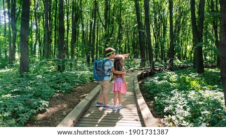 Family tourism concept. Children follow an organized hiking trail in a national park. The boy shows something interesting with surprise and delight. Ecotourism and environmental protection concept.