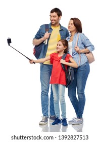 Family, Tourism And Travel Concept - Happy Smiling Mother, Father And Little Daughter With Backpacks Taking Picture By Smartphone On Selfie Stick Over White Background