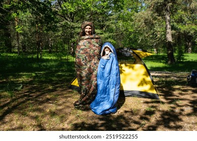 Family of tourists from a father and daughter pose and Funny dancing in sleeping bags near a tent. Family outdoor recreation, camping, hiking equipment.  - Powered by Shutterstock