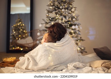 Family Traditions. Mother And Little Boy Son Watching Christmas Movie Or Tv With Popcorn At Home, Sitting Under Blanket In Cozy Room With Xmas Tree During Winter Holidays, Back View. Selective Focus