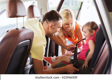 Family, Transport, Road Trip And People Concept - Happy Parents Fastening Child With Safety Belt In Baby Car Seat