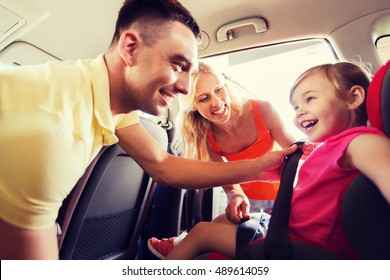 Family, Transport, Road Trip And People Concept - Happy Parents Fastening Child With Safety Belt In Baby Car Seat