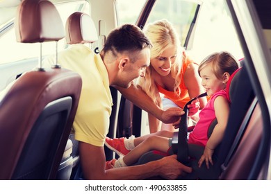 Family, Transport, Road Trip And People Concept - Happy Parents Fastening Child With Safety Belt In Baby Car Seat