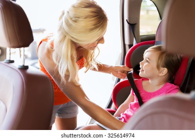 Family, Transport, Safety, Road Trip And People Concept - Happy Mother Fastening Child With Car Seat Belt