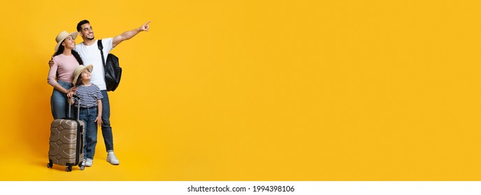 Family Travel Concept. Happy middle eastern parents with little daughter carrying suitcases and pointing aside at copy space on yellow background, mom, dad and child ready for vacation, panorama
