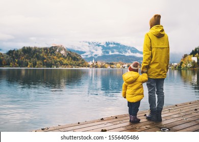 Family Travel Europe. Mother and child in yellow raincoats looking at Bled Lake. Autumn or Winter in Slovenia. View on Island with Church on Bled Lake with Castle and Mountains in Nature Background.