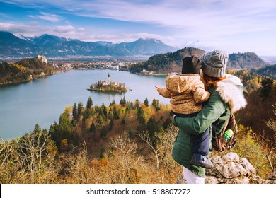 Family Travel Europe. Mother With Son Looking On Bled Lake. Autumn Or Winter In Slovenia, Europe. Top View On Island With Catholic Church In Bled Lake With Castle And Mountains In Background.