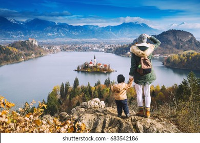 Family Travel Europe. Mother With Son Looking On Bled Lake. Autumn Or Winter In Slovenia, Europe. Top View On Island With Catholic Church In Bled Lake With Castle And Mountains In Background.