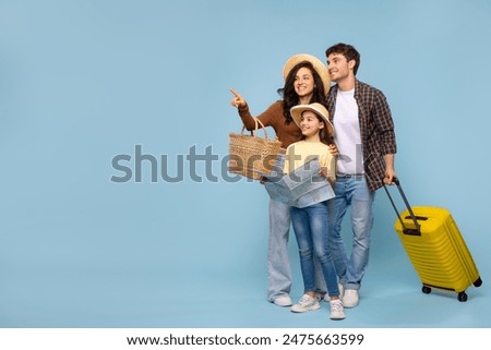 Family travel. Excited parents with daughter, man carrying suitcase and girl holding map, mother pointing aside at copy space on blue background