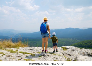 Family travel together in nature park, forest, mountains. Woman and kid boy on vacation. Traveler mother with child on top of high mountain outdoors, looking on beautiful landscape. Rear view.