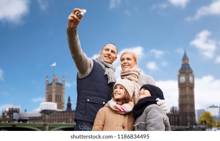 Family, Travel And Tourism Concept - Happy Mother, Father, Daughter And Son Taking Selfie By Camera Over Big Ben Tower In London City Background