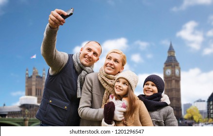 Family, Travel And Tourism Concept - Happy Mother, Father, Daughter And Son Taking Selfie By Smartphone Over Big Ben Tower In London City Background