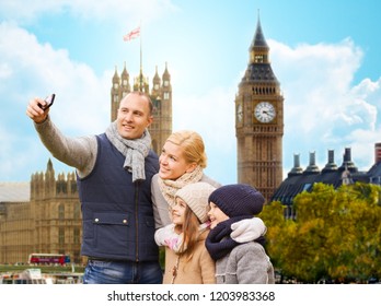 Family, Travel And Tourism Concept - Happy Mother, Father, Daughter And Son Taking Selfie By Smartphone Over Big Ben Tower In London City Background