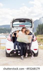 Family Traveling By Car And Using Paper Map To Navigate Sitting In Open Trunk