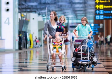 Family Traveling With Kids. Parents With Children At International Airport With Luggage In A Cart. Mother Holding Baby, Toddler Girl And Boy Flying By Airplane. Travel With Child For Summer Vacation.