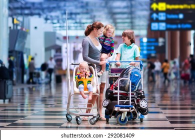 Family Traveling With Kids. Parents With Children At International Airport With Luggage In A Cart. Mother Holding Baby, Toddler Girl And Boy Flying By Airplane. Travel With Child For Summer Vacation.