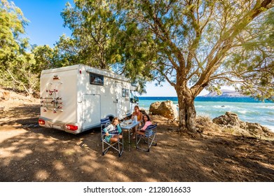 Family traveling with motorhome are eating breakfast on a beach. Travelers on an active family vacation with motorhome RV parked on the beach under a tree facing the sea, Crete, Greece. - Shutterstock ID 2128016633