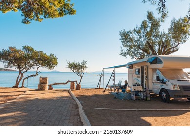 Family traveling with motorhome are eating breakfast on a beach. Travelers on an active family vacation with motorhome RV parked on the beach under a tree facing the sea, Crete, Greece.