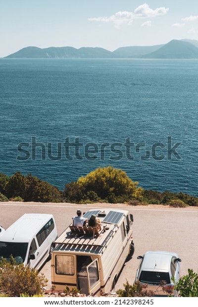 Family\
traveling with motorhome are eating breakfast on a beach. Travelers\
on an active family vacation with motorhome RV parked on the beach\
under a tree facing the sea, Crete,\
Greece.