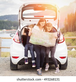 Family Travelling By Car And Using Paper Map To Navigate Sitting In Open Trunk