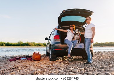 Family Of Two Person And Dog Sitting In Car Open Trunk And Have Fun