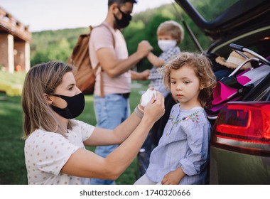 Family with two small children loading car for trip in countryside, wearing face masks.