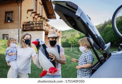 Family With Two Small Children Loading Car For Trip In Countryside, Wearing Face Masks.