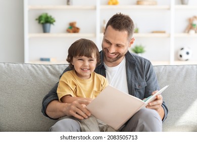 Family and upbringing concept. Close up portrait of happy little boy enjoying storytelling time with his daddy, sitting in armchair with big book - Powered by Shutterstock