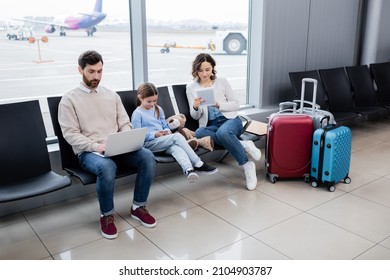 family using devices while sitting near luggage in airport lounge