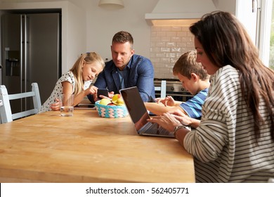 Family Using Digital Devices At Kitchen Table