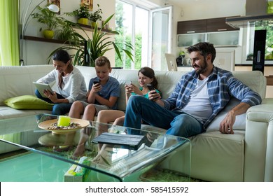 Family Using Laptop And Mobile Phone In Living Room At Home