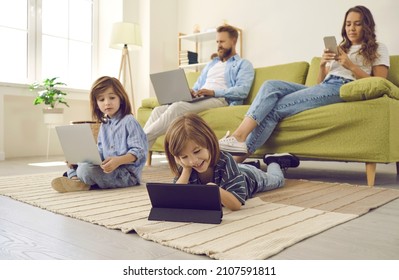 Family using modern devices. Little child lying on floor at home and holding digital tablet computer while his mom is using cellphone and brother and dad are using laptops. People, technology concept - Powered by Shutterstock