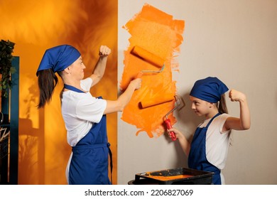 Family Using Orange Color To Paint Apartment Walls At Home, Painting Room Together With Roller Brush And Renovating Tools. Woman With Small Child Redecorating House, Decor Improvement.